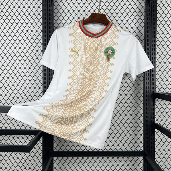 White t-shirt with gold patterns and a green emblem on a black metal rack.