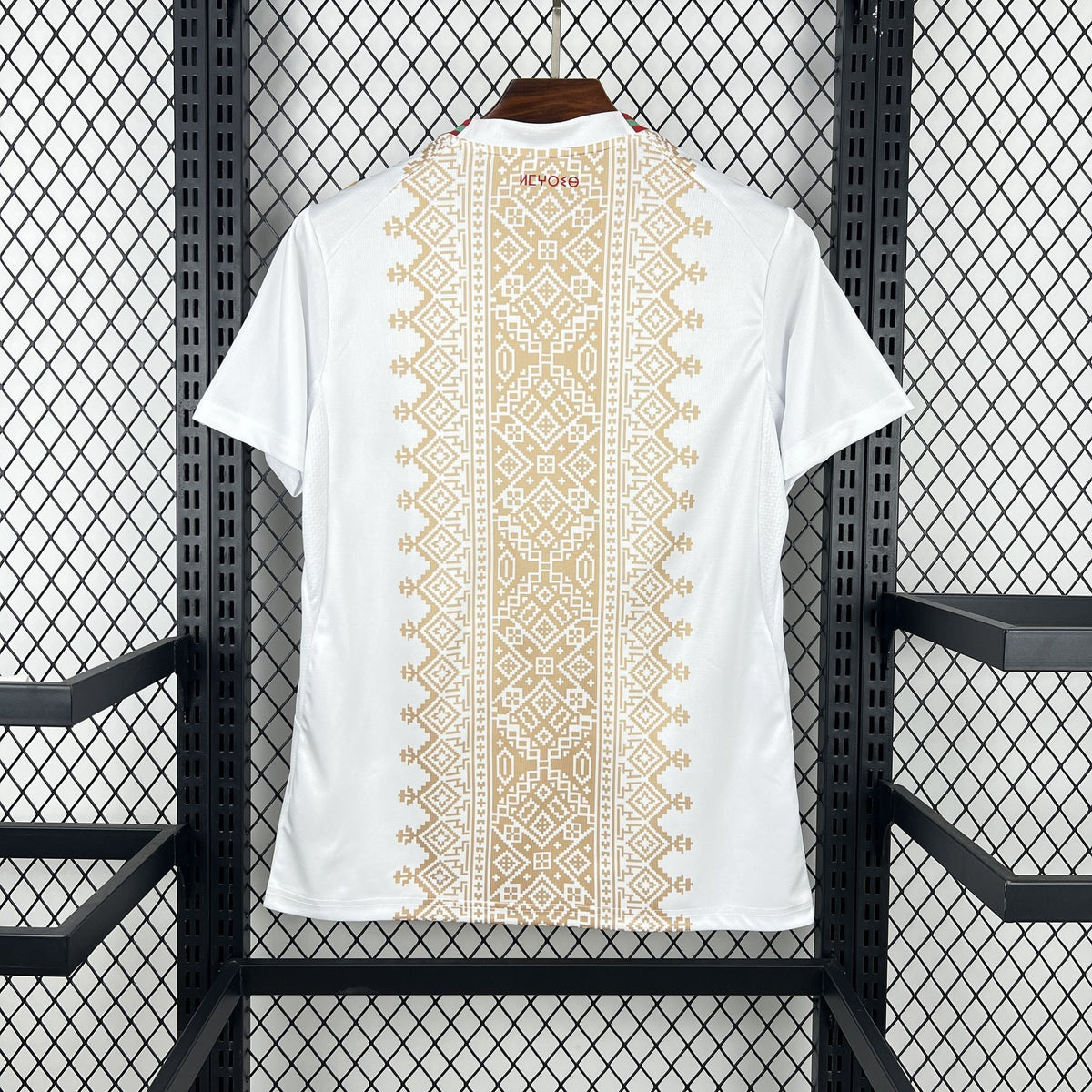 White t-shirt with gold geometric pattern on a hanger against a black metal grid background