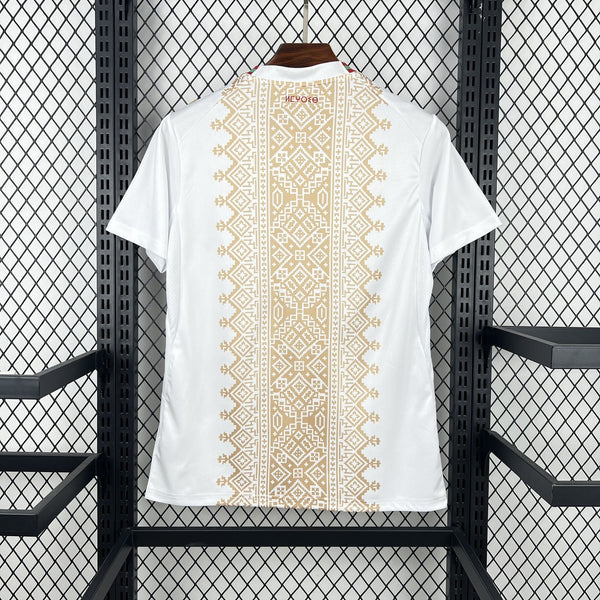White t-shirt with gold geometric pattern on a hanger against a black metal grid background