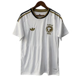 White t-shirt with Adidas logo and Saudi Arabia emblem on a hanger against a gray background
